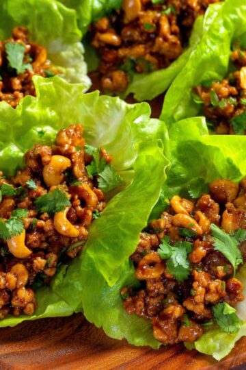 Easy Chicken Lettuce Wraps Recipe 2 Chicken Lettuce Wraps Recipe Chicken lettuce wraps filled with a savory mixture of ground meat, cashews, and flavorful sauce, topped with fresh cilantro. The wraps are neatly arranged in vibrant green lettuce leaves on a wooden platter.