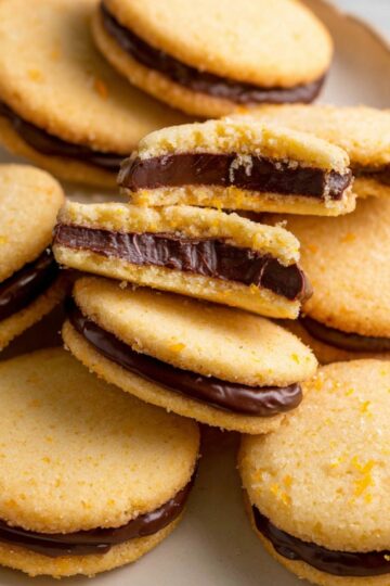 Best Chocolate Orange Sandwich Cookies 1 Chocolate Orange Sandwich Cookies A plate of orange butter cookies filled with chocolate ganache, some cookies slightly bitten to reveal the rich center.