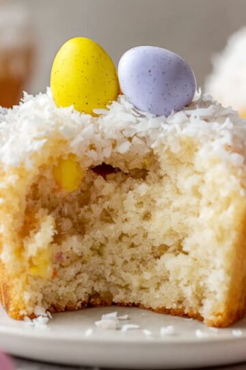 Healthy Coconut Easter Cupcakes Recipe 1 Coconut Easter Cupcakes A fluffy Easter cupcake with a coconut topping, sliced in half to reveal its soft, light interior, adorned with colorful Easter candy eggs on top