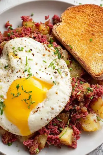 Easy Corned Beef Hash Recipe 2 Corned Beef Hash A plate of homemade corned beef hash, topped with a sunny-side-up egg and served with toasted bread.