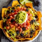 Dorito Taco Salad A close-up of a completed Dorito Taco Salad, showing layers of shredded cheese, black beans, tomatoes, black olives, and ground beef arranged in a white bowl. A side of creamy dressing sits next to the salad