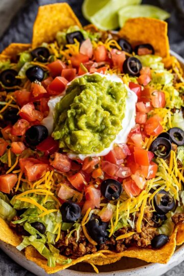The Best Dorito Taco Salad Recipe 2 Dorito Taco Salad A close-up of a completed Dorito Taco Salad, showing layers of shredded cheese, black beans, tomatoes, black olives, and ground beef arranged in a white bowl. A side of creamy dressing sits next to the salad