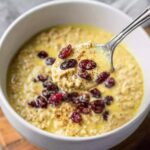 Golden Milk Overnight Oats A spoon scooping up creamy golden milk overnight oats, topped with cranberries, served in a white bowl.