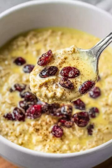 Best Golden Milk Overnight Oats Recipe 15 Golden Milk Overnight Oats A spoon scooping up creamy golden milk overnight oats, topped with cranberries, served in a white bowl.