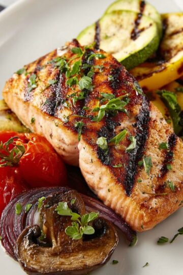 Delicious Grilled Salmon Recipe 5 A beautifully plated grilled salmon fillet served with grilled vegetables like zucchini, tomatoes, and mushrooms, garnished with fresh herbs