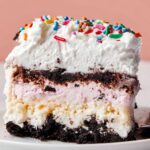 Ice Cream Cake The completed slice shows layers of the ice cream cake, including Oreo crumbs at the bottom, creamy layers in the middle, and a whipped topping with colorful sprinkles.