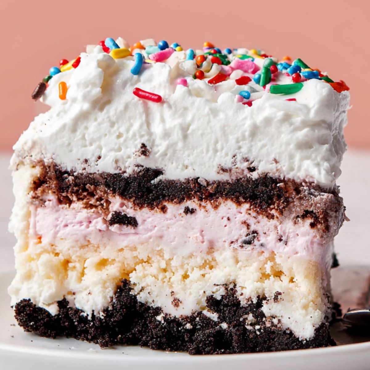 Ice Cream Cake The completed slice shows layers of the ice cream cake, including Oreo crumbs at the bottom, creamy layers in the middle, and a whipped topping with colorful sprinkles.