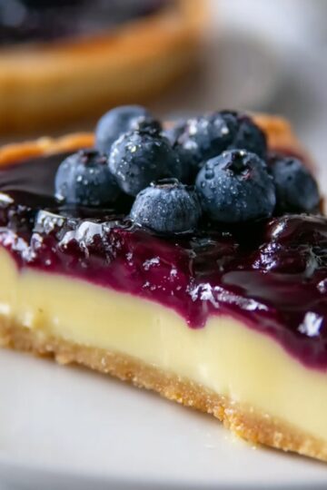 Easy Lemon Blueberry Tart Recipe 10 Lemon Blueberry Tart A beautifully sliced blueberry tart showing its layers. The tart has a golden, flaky crust with a luscious blueberry filling on top. A slice has been removed, revealing the smooth, fruit-filled interior.