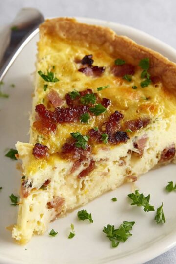 The Best Quiche Lorraine Recipe 2 Quiche Lorraine A slice of Quiche Lorraine served on a white plate with bacon and cheese filling, garnished with parsley.