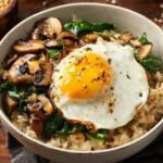 Savory Oatmeal A rustic food photography shot of a savory oatmeal bowl topped with a sunny-side-up egg, saut&eacute;ed mushrooms, and wilted spinach, served in a white ceramic bowl on a dark wooden table, natural light, shallow depth of field, high detail, warm tones, professional food styling.
