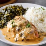 Smothered Chicken Recipe A serving of smothered chicken on a plate, topped with a creamy, flavorful sauce, served alongside a portion of fluffy white rice and cooked greens. The dish looks comforting and full of flavor.