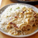 Smothered Pork Chops A beautifully plated serving of smothered pork chops, complete with a generous serving of creamy onion gravy over rice, making for a hearty, delicious meal.