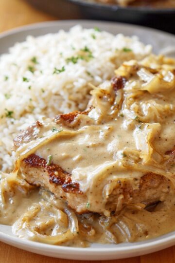 Easy Smothered Pork Chops Recipe 3 Smothered Pork Chops A beautifully plated serving of smothered pork chops, complete with a generous serving of creamy onion gravy over rice, making for a hearty, delicious meal.