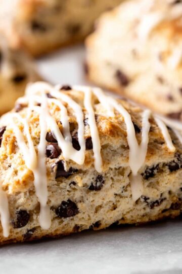 Best Sourdough Chocolate Chip Scones 1 Sourdough Chocolate Chip Scones Close-up of freshly baked chocolate chip scones drizzled with vanilla glaze, golden brown and flaky texture, soft interior with visible chocolate chunks, on a white surface, natural soft lighting, shallow depth of field, food photography, high resolution, cozy bakery style