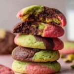 Spumoni Cookies A stack of freshly baked spumoni cookies with vibrant colors of green pistachio, red cherry, and dark chocolate. The cookies are dusted with sugar and one is broken in half, revealing the interior filled with the marbled dough.