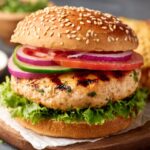 chicken burgers is assembled with a grilled chicken patty, fresh vegetables such as lettuce, tomato, and red onion, and placed in a sesame seed bun, ready to serve.