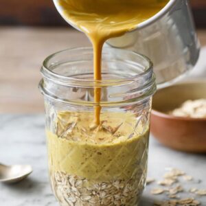 Golden milk being poured over a jar of oats, ready to soak and transform into a delicious breakfast.