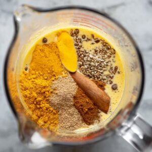 A close-up of golden milk ingredients, including turmeric, cinnamon, and other spices, arranged in a measuring cup.