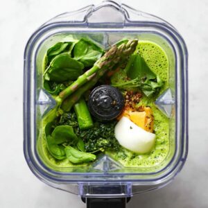 The Best Asparagus Soup Recipe 16 "A blender filled with fresh asparagus, spinach, and other ingredients, blending them together into a smooth soup base, ready to be cooked or served.