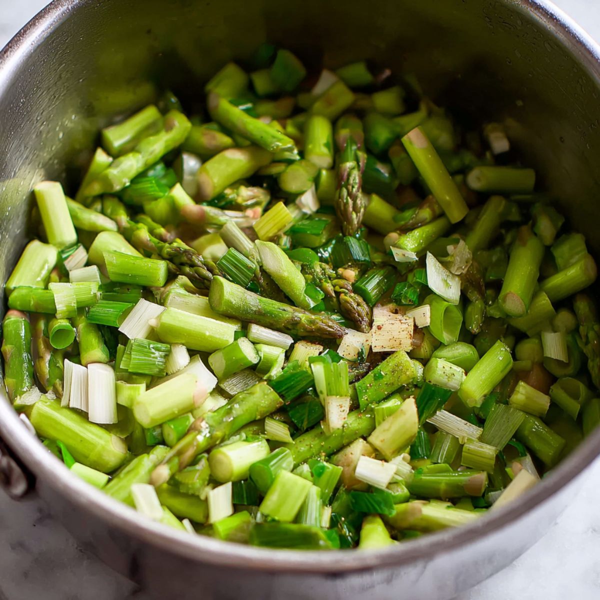 The Best Asparagus Soup Recipe 10 "Freshly chopped asparagus and green onions, seasoned with garlic and spices, ready to be sautéed together in a pot to create the base of a delicious asparagus soup.