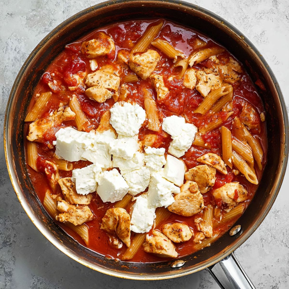 Best Buffalo Chicken Pasta Recipe 12 Chicken pieces in a skillet, with tomato sauce and a few dollops of cream cheese, ready to be mixed into the pasta