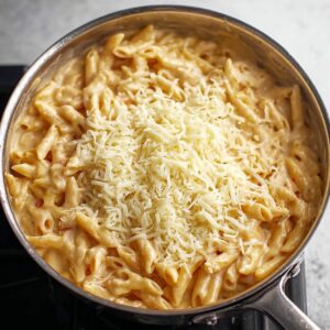 Best Buffalo Chicken Pasta Recipe 18 A creamy pasta dish in a skillet, topped with shredded cheese, ready to be melted and mixed into the sauce.