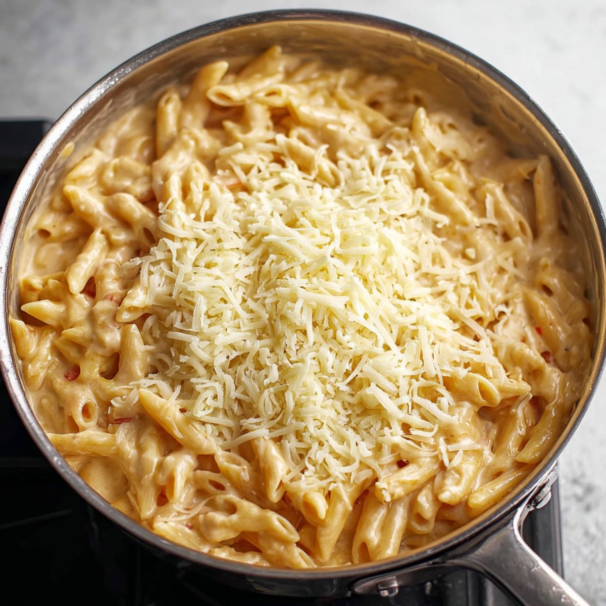 Best Buffalo Chicken Pasta Recipe 13 A creamy pasta dish in a skillet, topped with shredded cheese, ready to be melted and mixed into the sauce.
