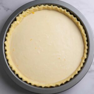 Best Buttermilk Pie Recipe 17 A pre-baked buttermilk pie with a smooth, creamy filling inside a crimped pie crust. The edges of the pie crust are neatly folded, and the filling is still uncooked, awaiting baking.