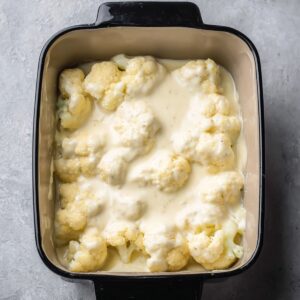 Best Cauliflower Gratin Recipe 15 Cauliflower florets arranged in a baking dish, covered with a creamy cheese sauce. The dish is prepared and ready to be baked until golden and bubbly.