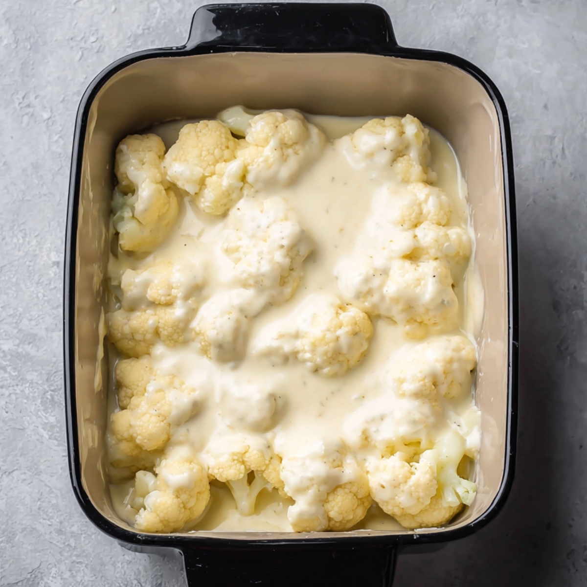 Best Cauliflower Gratin Recipe 12 Cauliflower florets arranged in a baking dish, covered with a creamy cheese sauce. The dish is prepared and ready to be baked until golden and bubbly.