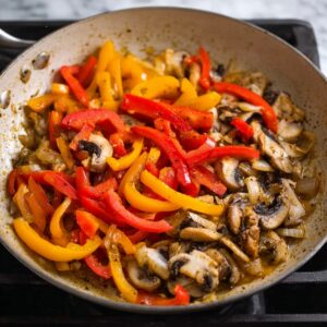 "Sautéed bell peppers, onions, and mushrooms cooking in a pan, creating a flavorful vegetable base for the chicken cacciatore.
