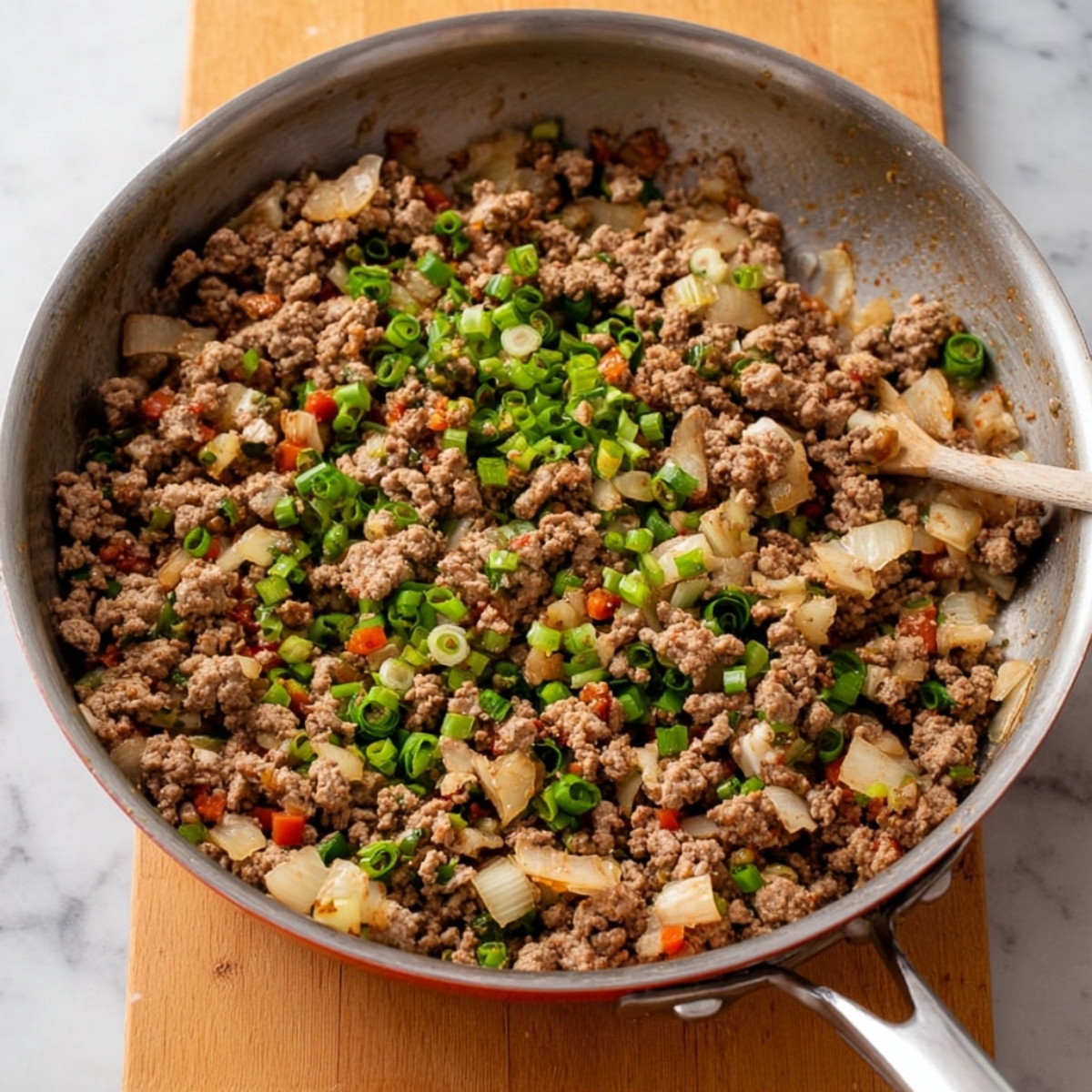 Easy Chicken Lettuce Wraps Recipe 11 A pan filled with cooked ground meat, vegetables, and green onions, ready to be used for chicken lettuce wraps.