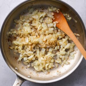 Easy Chicken Lettuce Wraps Recipe 14 Sliced mushrooms being sautéed in a skillet, with a wooden spoon stirring them as they release moisture and cook down.