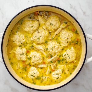 Healthy Chicken and Dumplings with Biscuits 16 Turkey and dumplings simmering in a large pot, with the dumplings nestled in a flavorful broth. The vibrant yellow liquid highlights the rich textures of the turkey and the soft, pillowy dumplings, ready to be enjoyed.