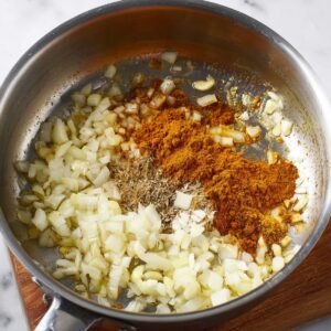 Delicious Chickpea Curry Recipe 15 A stainless steel pan with chopped onions, garlic, and curry powder being sautéed, with the rich aroma of spices starting to blend into the mix