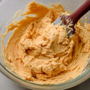 Best Chocolate Orange Sandwich Cookies 15 Close-up of orange butter cookie dough with a spatula, showing the smooth texture before baking.