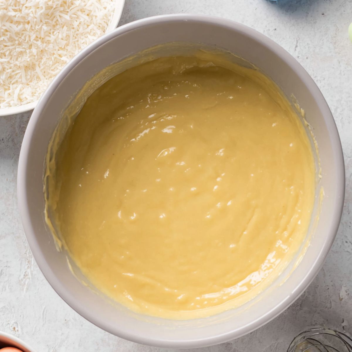 Healthy Coconut Easter Cupcakes Recipe 10 A mixing bowl with smooth cupcake batter, ready to be poured into liners, accompanied by a bowl of shredded coconut and pastel candy eggs, perfect for Easter cupcakes.