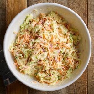 Healthy Coleslaw Recipe Recipe 16 Overhead view of a white bowl filled with creamy coleslaw made of shredded cabbage and carrots on a rustic wooden table.