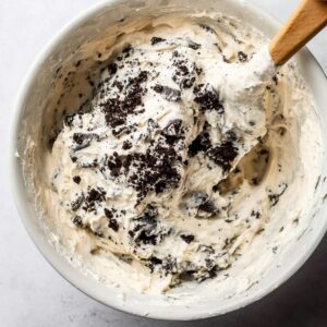 A mixing bowl filled with creamy mixture and crumbled Oreo cookies, being stirred with a spatula, ready to be poured into the pie crust.