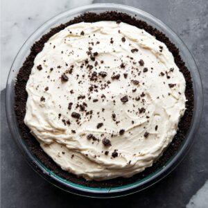 A glass pie dish filled with a smooth cream layer atop an Oreo cookie crust, ready to be set or served. The creamy texture contrasts beautifully with the dark crust.