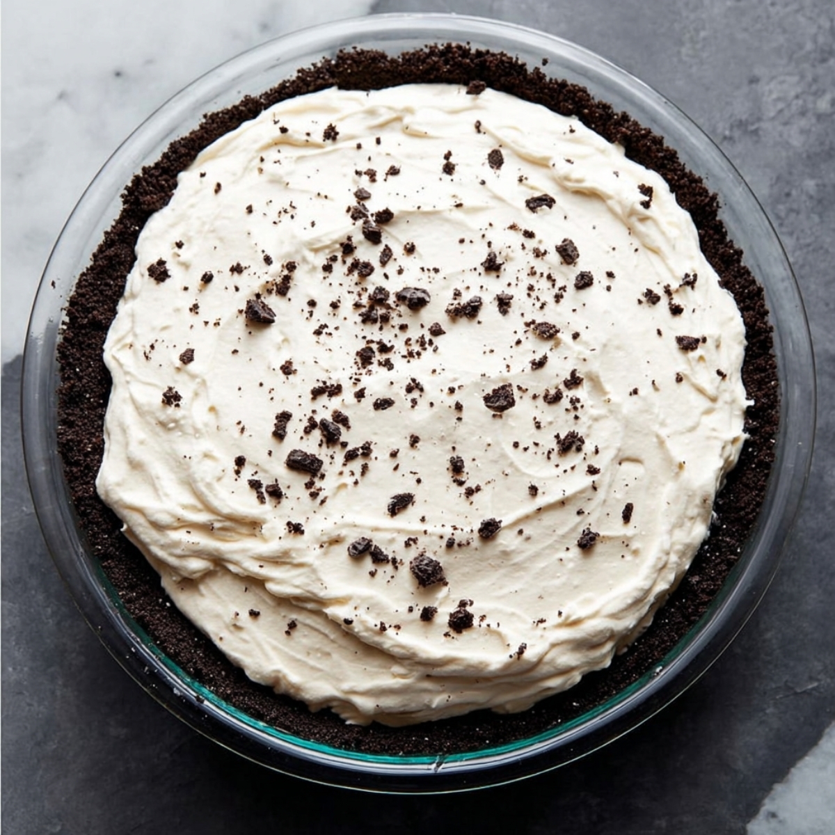 Easy Cookies and Cream Pie Recipe 13 A glass pie dish filled with a smooth cream layer atop an Oreo cookie crust, ready to be set or served. The creamy texture contrasts beautifully with the dark crust.