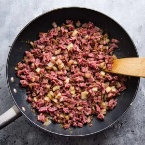 Easy Corned Beef Hash Recipe 16 Sautéed corned beef mixed with potatoes, cooked in a skillet, with seasoning and fresh herbs.