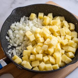 Easy Corned Beef Hash Recipe 17 Diced potatoes and onions in a pan, ready to be sautéed for corned beef hash.