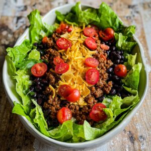 The Best Dorito Taco Salad Recipe 15 A Dorito Taco Salad with a base of crisp lettuce, black beans, cherry tomatoes, and seasoned ground beef, topped with shredded cheese. The salad is beautifully arranged with vibrant, fresh ingredients.