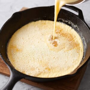 Pouring pancake batter into a hot skillet, ready for baking