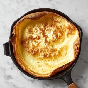A perfectly golden, puffy Dutch baby pancake fresh from the oven in a cast iron skillet.