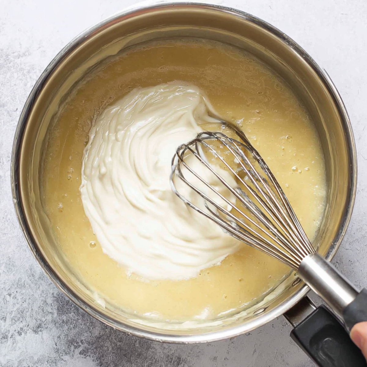 Healthy Ham and Potato Soup Recipe 11 Image showing the process of adding cream to a saucepan, with a whisk stirring it in to create a smooth, creamy texture for the soup.
