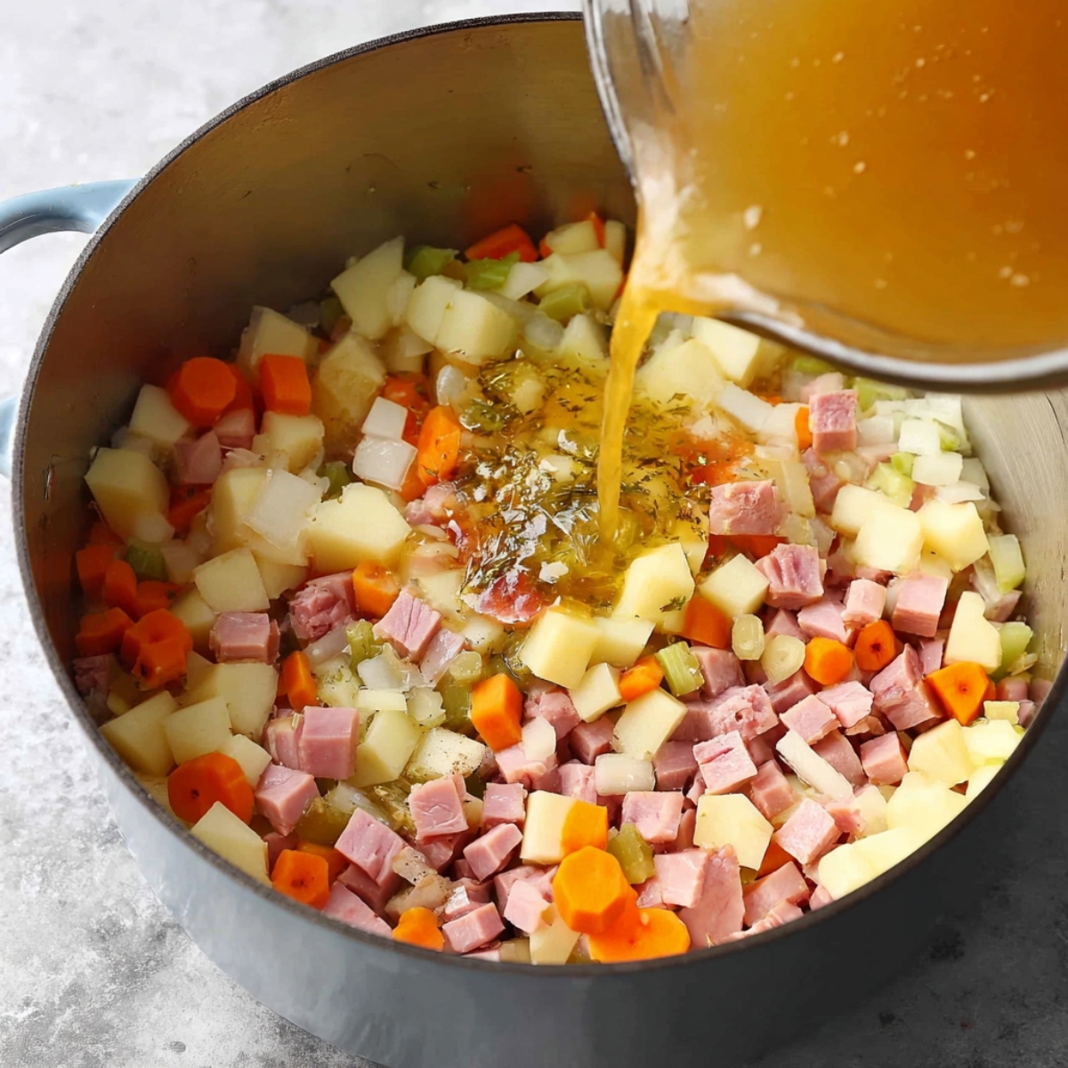 Healthy Ham and Potato Soup Recipe 10 Image of a pot with diced ham, potatoes, and vegetables, with broth being poured in, indicating the start of a flavorful soup or chowder.