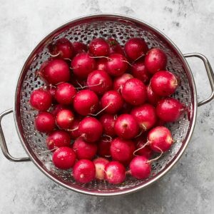Easy Roasted Radishes Recipe 14 "A colander filled with fresh, unwashed radishes, showcasing their bright red skin. The radishes are clean and round, ready for the next step in the cooking process."