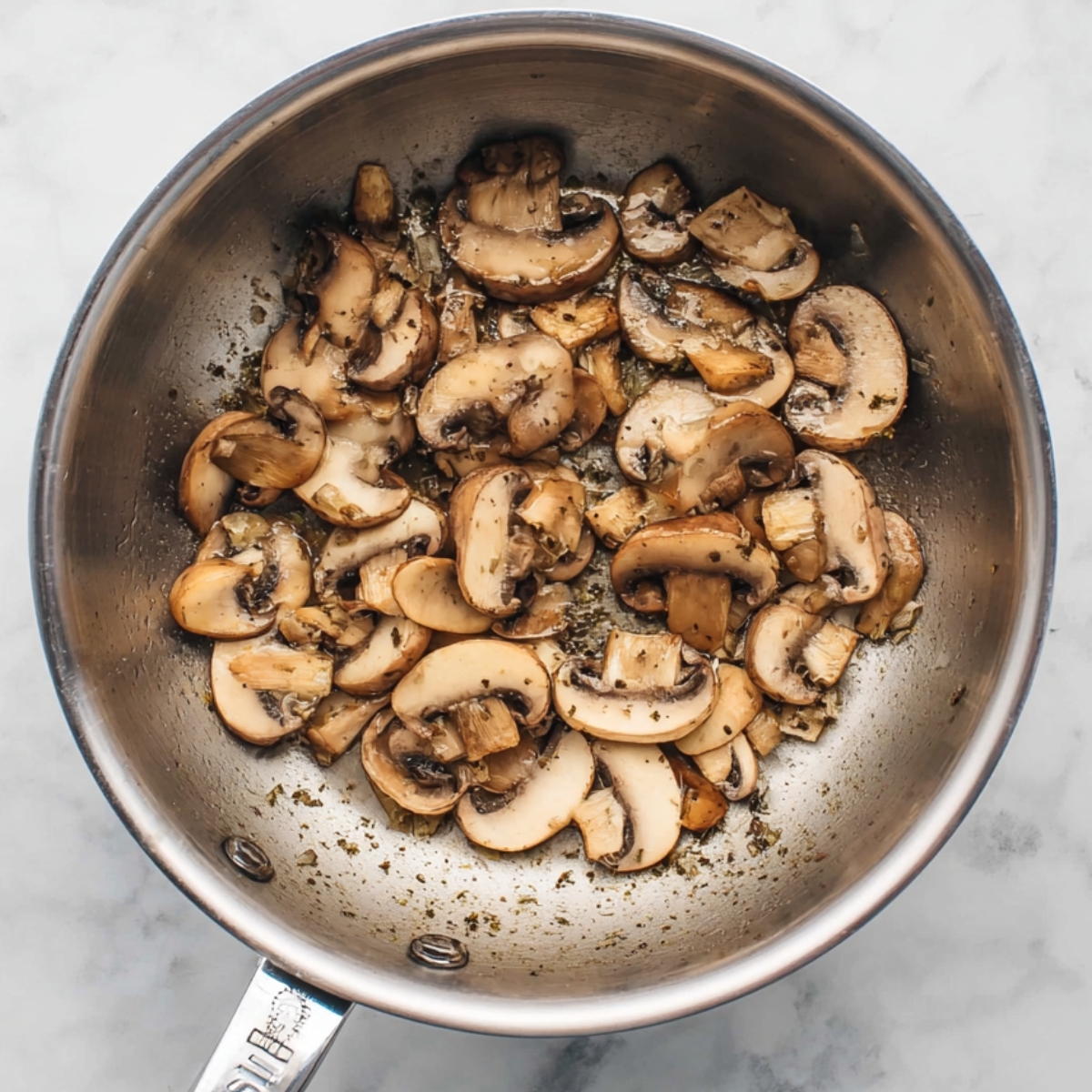 Easy Savory Oatmeal Recipe 10 A top-down view of sliced mushrooms being sautéed in a stainless steel saucepan, lightly browned, simple cooking scene, white marble background, natural lighting, realistic texture, clean and minimal food photography.